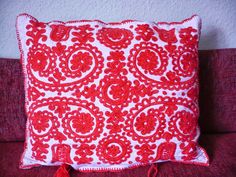 a red and white pillow with tassels on the back sitting on a couch