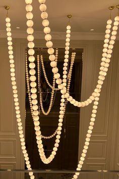 some lights that are hanging from the ceiling in front of a mirror with beads on it