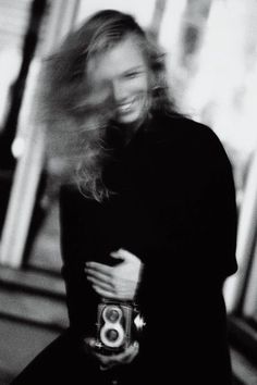 black and white photograph of a woman holding a camera with blurry hair in the background