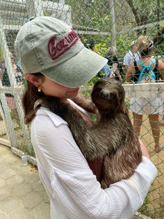 a woman holding a baby sloth in her arms