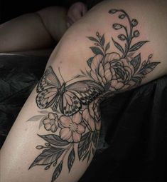 a woman's thigh with flowers and a butterfly tattoo on her leg, while she is laying down