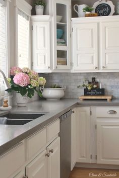 a kitchen with white cabinets and flowers on the counter top in front of an open window