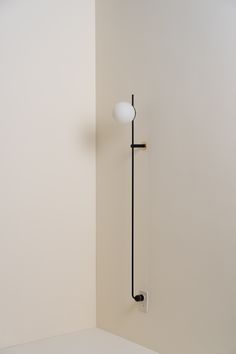 a white wall with a black pole and a light on it's side in the corner