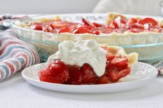 a slice of strawberry pie on a plate with whipped cream and strawberries in the background