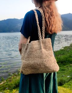 a woman with long red hair is carrying a straw bag near the water's edge