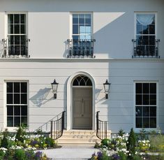 a large white house with lots of windows and plants in front of the entrance to it