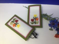 two cross - stitch bookmarks sitting on top of a table next to a flower vase