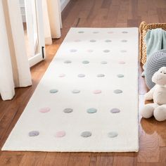 a teddy bear sitting on the floor next to a white rug with polka dot design