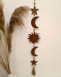 a metal sun and moon hanging on the wall next to some dried grass in a vase