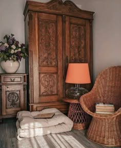 a wicker chair sitting next to a wooden armoire with a lamp on it