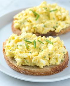 two pieces of bread topped with scrambled eggs on top of a white plate and garnished with chives