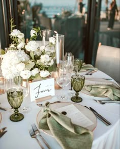 the table is set with white flowers and place settings