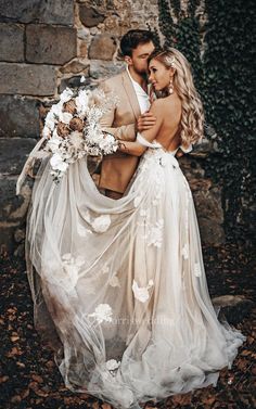 a bride and groom standing in front of a stone wall holding each other with their arms around each other