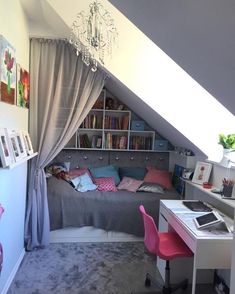 a bedroom with a bed, desk and chair under a slanted ceiling that has a chandelier hanging from it