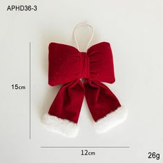 a red bow ornament hanging on a white wall next to a measuring ruler