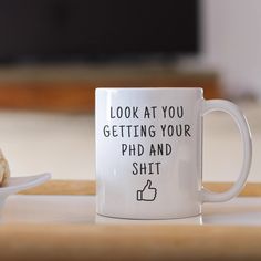 a white coffee mug sitting on top of a wooden table next to a donut