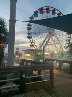 the ferris wheel is lit up at night on the boardwalk near an amusement park area