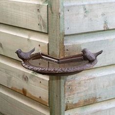 two birds are perched on the handle of a bird bathtub that is attached to a wooden building