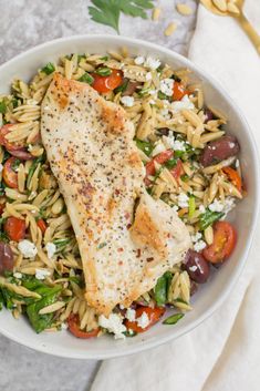 a white bowl filled with pasta salad and fish on top of a table next to a fork