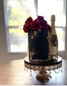 a black and gold decorated cake with red roses on the top, next to a bottle of champagne