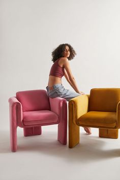 a woman sitting on top of a chair next to a pink and yellow chair in front of a white wall