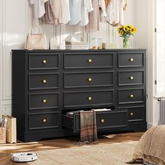 a black dresser with gold knobs and clothes hanging on the wall next to it