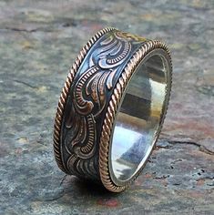 a silver ring with an intricate design on the outside and inside, sitting on top of a rock