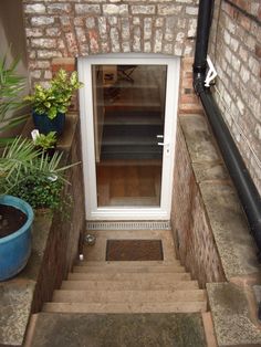 an open door on the side of a brick building next to plants and potted plants