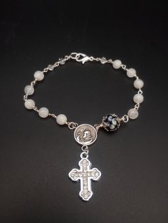 St Padre Pio Rosary Bracelet Style of Bracelet: one decade of ave marias, a pater noster bead, a medal and a crucifix Size: 7 1/2 inches Medal: San Padre Pio doubles sided medal Crucifix: white goldplated cross with Rhine stones. Chain: .925 silver plated Ave maria beads: 6mm moonstone polished Pater Noster Bead: this is a handmade bead by Etsy lampwork artist Annie Alta, it is dark blue with little calla lilies, encased in two silver plated leaf bead caps. Feast Day: Sept 23. Spiritual Rosary Bracelet With Miraculous Medal, Elegant Rosary Bracelet With Miraculous Medal, Elegant Rosary Bracelet With Miraculous Medal Gift, Miraculous Medal Bracelet Jewelry Gift, White Miraculous Medal Spiritual Jewelry, Elegant White Cross Bracelets, Elegant White Cross Bracelet, Adjustable Elegant Rosary, Elegant Adjustable Rosary