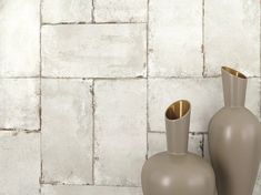 two gray vases sitting next to each other in front of a white brick wall