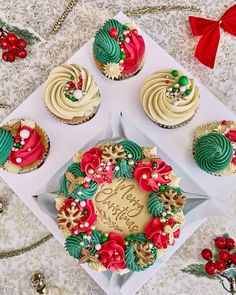 cupcakes with frosting and decorations on top of a white box, surrounded by christmas decorations