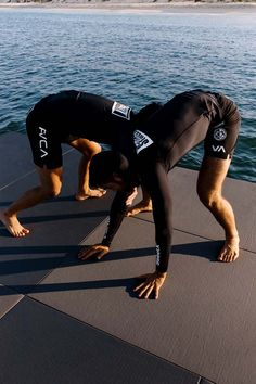 two men in wetsuits doing yoga on a dock