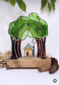 a stained glass house with a tree and pine cone on the ground next to it