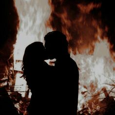 a couple standing in front of a fire with their arms around each other and kissing