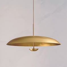 a gold colored pendant light hanging from a ceiling in a room with white walls and flooring