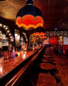 a dimly lit bar with wooden stools and colorful lights hanging from the ceiling above