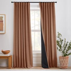 a living room with a large window covered in curtains and a potted plant next to it