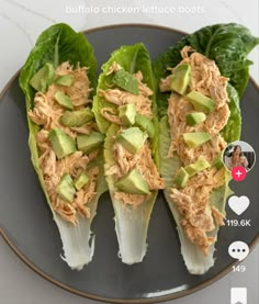 three lettuce wraps with shredded chicken and avocado on top, sitting on a black plate