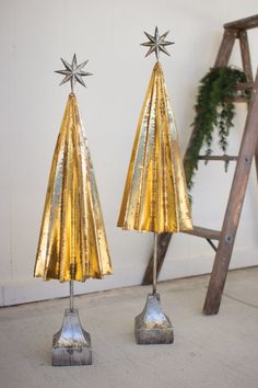 two metal christmas trees sitting next to each other on top of a cement floor in front of a ladder