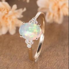 a white opal and diamond ring sitting on top of a table next to flowers