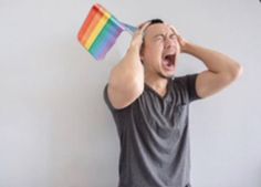 a man is holding a rainbow flag and screaming with his mouth wide open while standing in front of a white wall