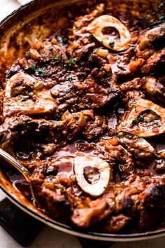 a skillet filled with meat and mushrooms on top of a white countertop next to utensils