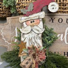 a wooden sign with a santa clause on it's face and some greenery