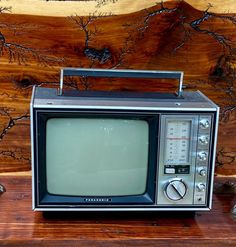 an old fashioned tv sitting on top of a wooden table next to a tree branch