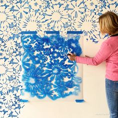 a woman is painting on a wall with blue flowers and leaves in the process of being stencilled