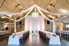 an indoor wedding venue with white draping and chandelier draped over the tables