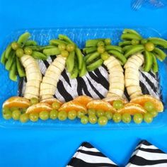 a plastic container filled with bananas, oranges and green grapes on top of zebra print napkins