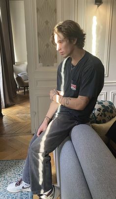 a young man sitting on top of a couch in a living room next to a window