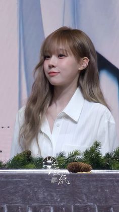 a woman with long hair and bangs standing in front of a screen wearing a white shirt