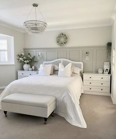 a white bed sitting under a chandelier in a bedroom next to a window